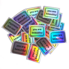 You Are Beautiful holographic sticker pack cover shot with rainbow shine on a notebook