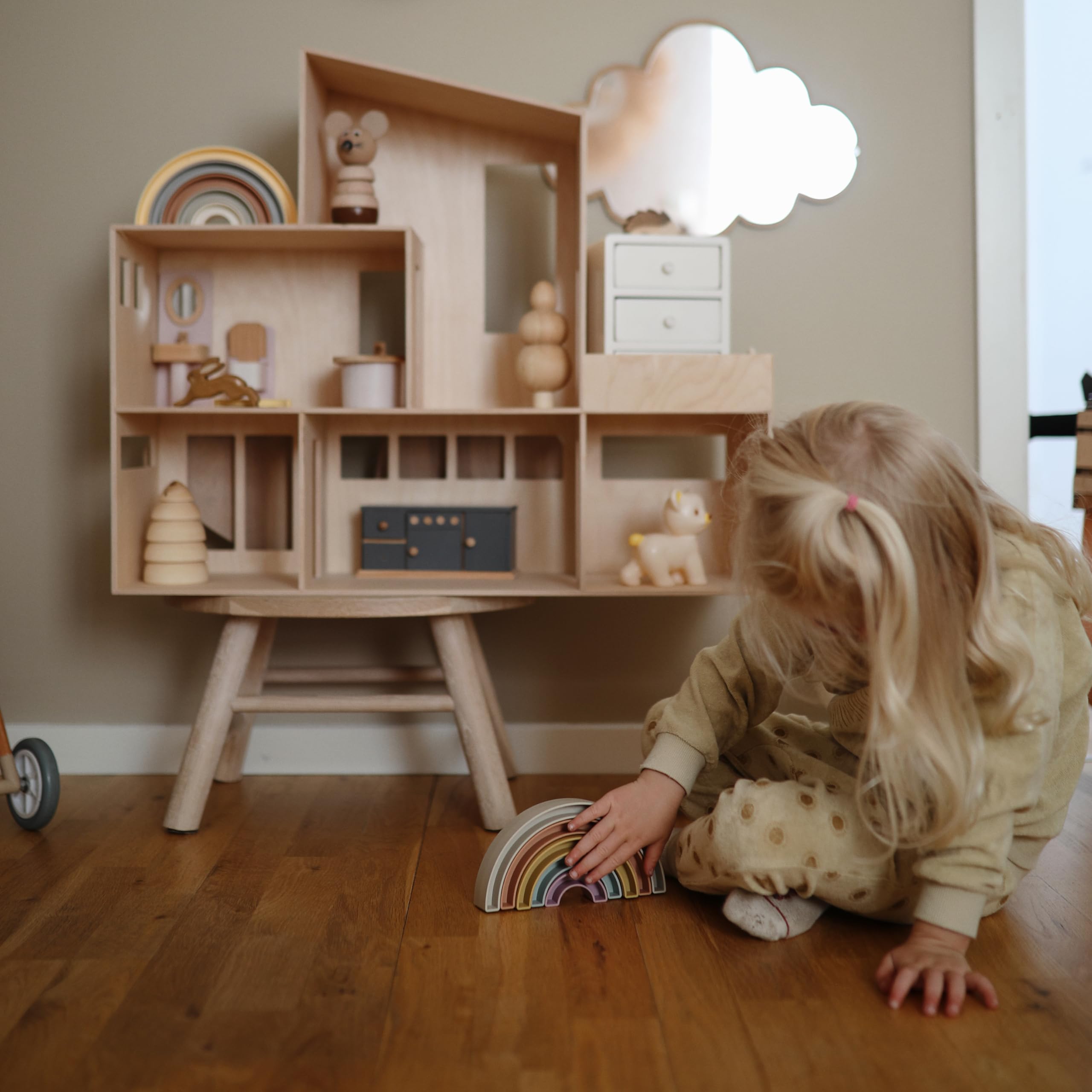 Mushie rainbow stacker in use, child stacks blocks to explore balance.