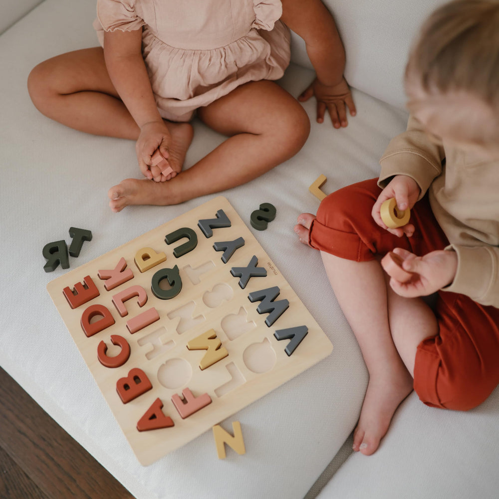 Mushie wooden alphabet puzzle kid hands using the pieces.
