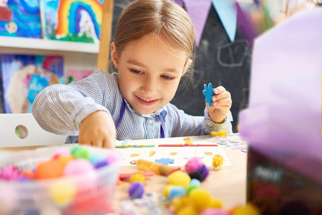 Olly Kids crafting indoors with glue, stickers, and color supplies.